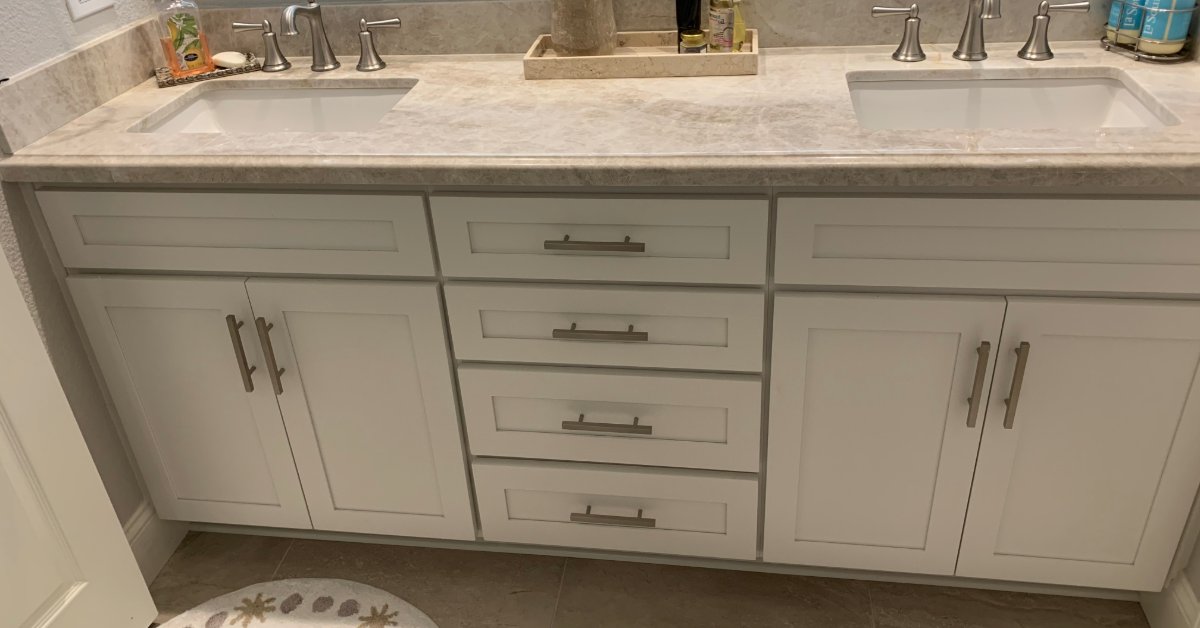 A bathroom vanity with gray cabinets, silver handles, a white countertop, sinks, faucets, and a tile floor.